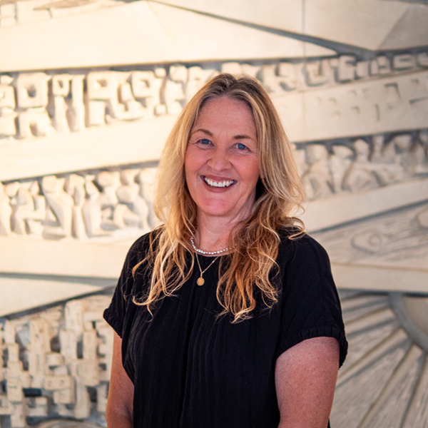 Head and shoulders portrait of Ginny, wearing a black top, standing in front of a textured light-coloured background.