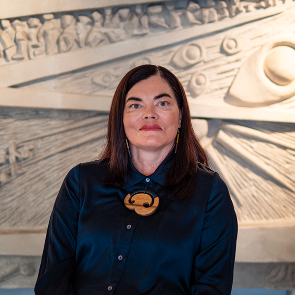 Head and shoulders portrait of Ronelle, wearing a black top, standing in front of a textured light-coloured background.