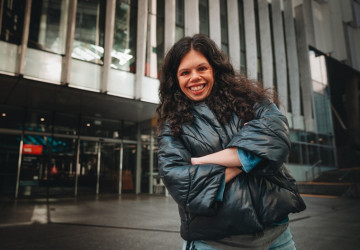 Young woman standing and smiling in front of a building.