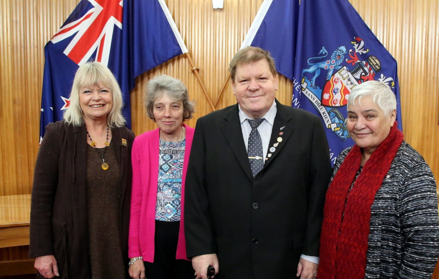 Former Whanganui mayor Annette Main, Lady Lynda and Sir Robert Martin with Dame Tariana Turia standing together smiling in front of a wooden panelled wall with two flags (one being the NZ flag)