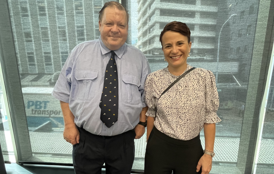 Sir Robert Martin stands with Paula Tesoriero in front of a large window at the Whaikaha office at the launch of My Home, My Choice. They are both smiling and looking at the camera.